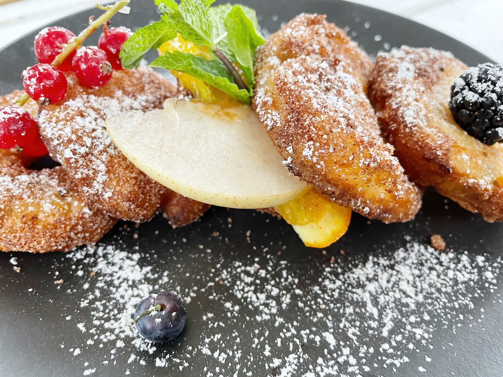 Apfelküchle in Zimtzucker mit Puderzucker, Birne und frischen Beeren auf schwarzem Teller